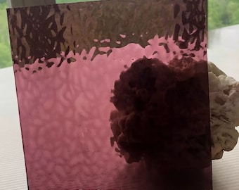 Puede incluir: Un trozo cuadrado de vidrio texturizado con un tono morado oscuro. El vidrio tiene una superficie ondulada y desigual.