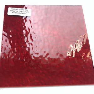 May include: A sheet of red, transparent glass with a wavy, textured surface. The glass is labeled "Wissmach Copper Red Transparent English Muffle from Mead Dog Mosaics".