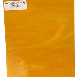 May include: A sheet of yellow streaky opal glass. The glass is translucent and has a slight shimmer. The label reads "Yellow Sunshine Opal Streaky Tiffany Today From Mixed Bag Mosaics".