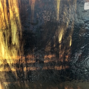 May include: A piece of dichroic glass with a dark brown and gold color scheme. The glass has a swirling pattern with streaks of gold and brown.