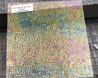 May include: A sheet of iridescent clear glass with a dew drop texture. The glass is labeled "Clear Iridescent Dew Drop Wesmach From Mixed Bag Mosaics".