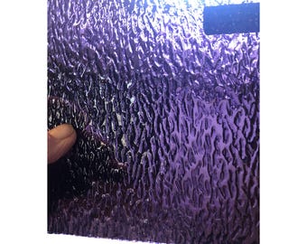 Puede incluir: Una lámina de vidrio texturizado con un acabado iridiscente morado. El vidrio tiene un patrón ondulado.