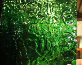 May include: Close-up of a textured, emerald green glass sheet. The glass has a rippled, organic pattern, creating a dynamic and reflective surface. The color is a deep, rich green, with highlights and shadows adding depth.