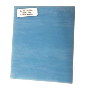 May include: A sheet of light blue glass with a white label that reads "Sky Blue Opal Wavy Tiffany Today from Mixed Bag Mosaics".