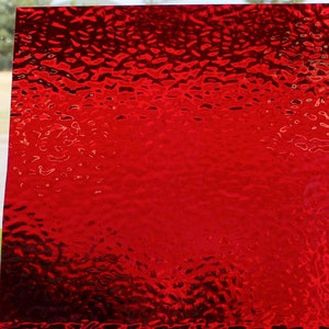 May include: A sheet of textured red glass. The surface has a pattern of small, irregular shapes, creating a dynamic visual effect. The color is a deep, vibrant red, with variations in tone across the surface. The glass is likely used for decorative purposes.