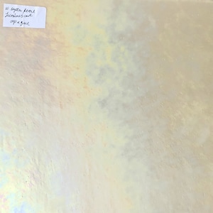 May include: A close-up of a white iridescent tile with a subtle yellow hue. The tile has a textured surface and a slight shimmer. The text "W oyster pearl luminescent opaque" is written on a white label.