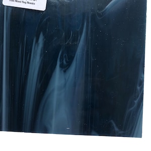 May include: A square piece of stained glass with a dark blue base and swirling white and light blue patterns. The glass has a glossy finish and is likely for mosaic or craft projects.
