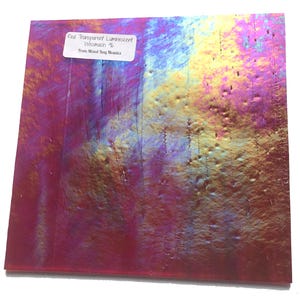 May include: A square piece of red, transparent, iridescent glass with a textured surface. The glass has a luminescent quality, with areas of yellow, purple, and blue. A white label in the upper left corner reads "Red Transparent Luminescent Wissmach % From Mixed Bag Mosaics."