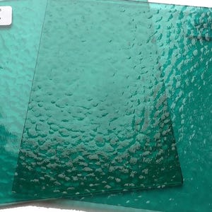 May include: Two sheets of textured, teal-colored glass. The glass has a bumpy, uneven surface.