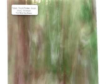 May include: A sheet of glass mosaic tiles with a wispy, swirled pattern in shades of purple and green. The text "Medium Purple/Medium Green Wispy Wissmach From Mixed Bag Mosaics" is printed on a white label in the top left corner.