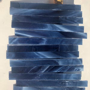 May include: A stack of dark blue glass tiles with a white swirl pattern. The tiles are approximately 1/2 inch wide and 6 inches long.