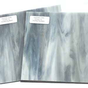 May include: Two square glass tiles with a marbled gray and white pattern. Each tile has a label that reads "Gray/White Prima Wisconsin % From Mixed Bag Mosaics". The tiles are likely for mosaic art projects.