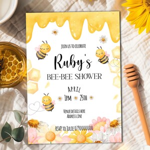 Op de afbeelding: Een gele en witte babyshower-uitnodiging met een bijen-thema. De uitnodiging luidt "Doe mee met de viering van Ruby's Bee-Bee Shower" met de datum en tijd van het evenement. De uitnodiging is versierd met honingraten, bijen en bloemen.