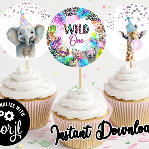 May include: Three cupcake toppers featuring a watercolour illustration of a giraffe, elephant, and a jungle scene with the text "Wild One". The toppers are on top of cupcakes with white frosting.