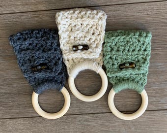 May include: Three crocheted dishcloths with wooden rings. The dishcloths are in gray, white, and green.