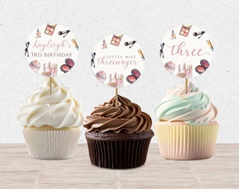 May include: Three cupcakes decorated with round, white, printable cupcake toppers featuring a makeup theme. The toppers have pink and gold accents and include the text "Kayleigh's 3rd Birthday", "Little Miss Three-nager", and "three".