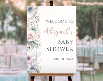 May include: Welcome to Abigail's Baby Shower sign with a floral design in shades of blue, pink, and green. The sign is on an easel and the text is in a dark blue font. The date of the shower is June 8, 20XX.