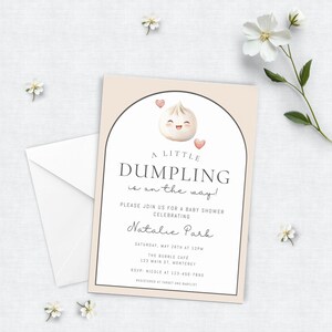 May include: Baby shower invitation with a dumpling illustration. The invitation features the text "A Little Dumpling is on the way!" and details for the event, including the date, time, and location. A white envelope and floral accents complete the design.