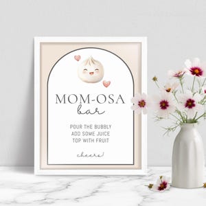 May include: A framed sign with the text "MOM-OSA bar" and instructions for a cocktail. The sign features a cartoon dumpling with a smiling face and two pink hearts. A vase of white and pink flowers sits to the right.