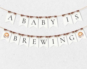 May include: A banner with white pennants strung on twine. The top banner reads "A BABY IS" and the bottom banner reads "BREWING" in black letters. Coffee beans and coffee cup illustrations decorate the banner.