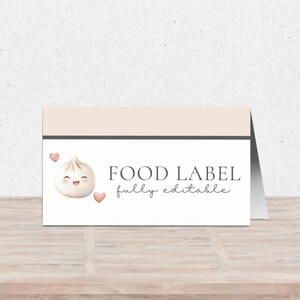 May include: A folded food label with a light beige top and a white base. The label features a smiling dumpling illustration with two pink hearts. Text reads "FOOD LABEL fully editable."