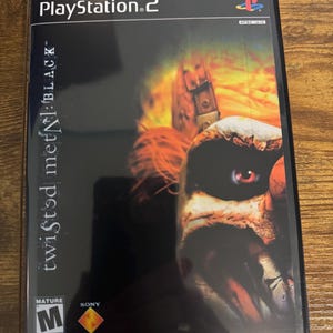 May include: A PlayStation 2 video game case for Twisted Metal: Black. The cover features a dark background with a close-up of a clown face with red eyes and orange hair. The text includes the PlayStation 2 logo, ESRB M rating, and Reprinted Art.