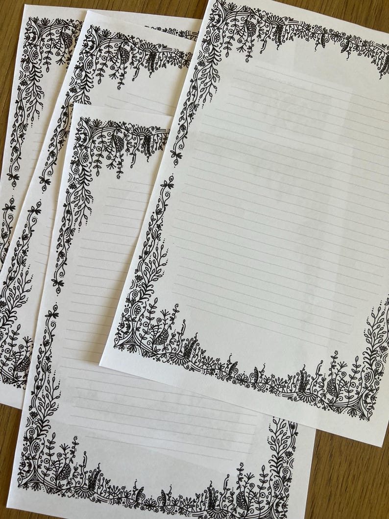 Peut inclure: Trois feuilles de papier &agrave; lettres blanc avec des bordures botaniques dessin&eacute;es &agrave; l'encre noire. Chaque page pr&eacute;sente des lignes horizontales pour l'&eacute;criture, entour&eacute;es d'illustrations complexes de vignes, de feuilles et de fleurs.