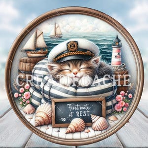 Puede incluir: Ilustración de temática náutica con un gato durmiente con gorro de capitán y camisa a rayas. El gato está en un marco de madera redondo, rodeado de conchas marinas, un faro y un pequeño velero. Un letrero de pizarra dice "First mate at REST."