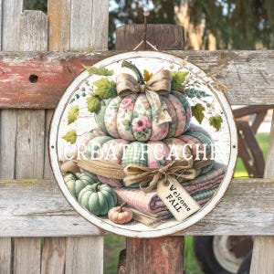 Puede incluir: Un letrero redondo de metal blanco con temática otoñal. El letrero presenta una calabaza grande con estampado floral con un lazo, calabazas más pequeñas y el texto "CREATIFCACHE". Una etiqueta dice "Welcome FALL". El letrero está colgado en una valla de madera.