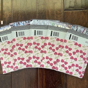 May include: Five pink and white poly mailers with a cherry print. The mailers are made of a bubble-lined material and have a self-adhesive closure.