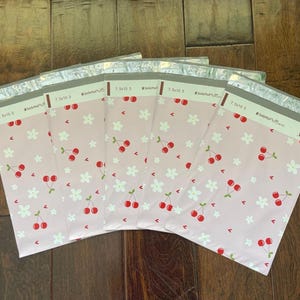 May include: Six pink and white patterned mailing envelopes with the text "SmileMail by Claire" and "7.5 x 10.5" printed on them. The envelopes feature a repeating pattern of white flowers and red cherries.