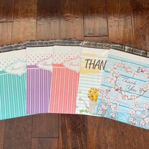 May include: A collection of colorful poly mailer envelopes with "Thank You" and "Thank" messages. Designs include vertical stripes, floral wreaths, and a watering can with flowers. The envelopes are in shades of teal, purple, coral, yellow, and blue.
