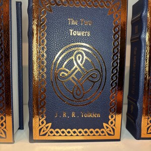 K&ouml;nnte beinhalten: Ein marineblaues Buch mit dem Titel "The Two Towers" von J.R.R. Tolkien, mit goldenen Details. Das Cover zeigt ein goldenes Muster und einen Rand. Der Buchr&uuml;cken ist ebenfalls sichtbar, mit dem Titel "The Return of the King".