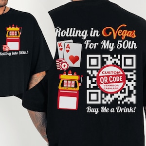 May include: Black t-shirt with the text "Rolling in Vegas For My 50th" and a custom QR code. The design includes playing cards, casino chips, and a slot machine graphic. The front of the shirt has a slot machine graphic and the text "Rolling into 50th!"