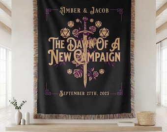 Può includere: Coperta nera con un design dorato e viola. Il testo recita "Amber & Jacob" e "The Dawn Of A New Campaign" con la data "27 settembre 2025". Il design include dadi, rose e una spada.