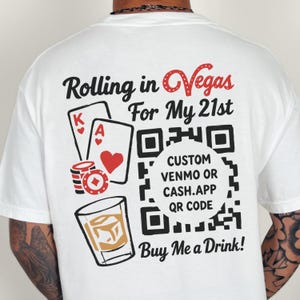 May include: A white t-shirt featuring a back graphic with the text Rolling in Vegas For My 21st and Buy Me a Drink. The design includes playing cards, a stack of poker chips, a glass of whiskey, and a large QR code with the text CUSTOM VENMO OR CASH.APP QR CODE.