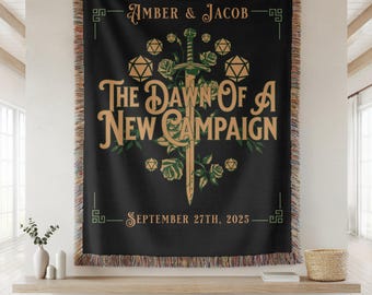 Può includere: Coperta nera con un design decorativo con spada, rose e dadi. Il testo recita "AMBER & JACOB" e "THE DAWN OF A NEW CAMPAIGN SEPTEMBER 27TH, 2025". La coperta ha un bordo sfrangiato.