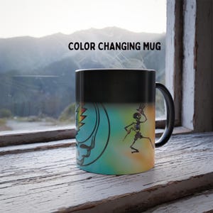 May include: Color-changing mug with a black handle and rim. The mug features a colorful design with a skull and lightning bolt, and a dancing skeleton. The text "COLOR CHANGING MUG" is printed on the mug.