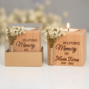 May include: Two wooden memorial candle holders with the text "IN LOVING Memory OF" and a name and dates. One candle is lit. Each holder has a small bouquet of dried flowers.