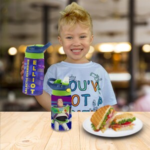 May include: A purple and green water bottle with the name "ELLIOT" and the words "GALACTIC GUARDIAN". The bottle also has a Buzz Lightyear graphic. The child is wearing a white t-shirt with the words "YOU'VE GOT A FRIEND IN ME".