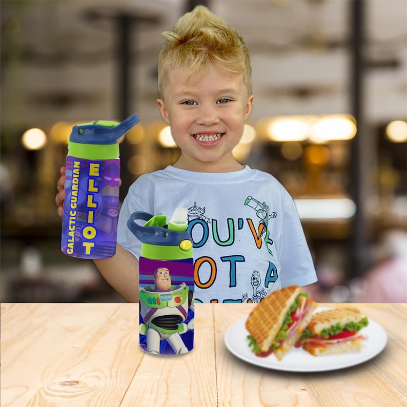 May include: A purple and green water bottle with the name "ELLIOT" and the words "GALACTIC GUARDIAN". The bottle also has a Buzz Lightyear graphic. The child is wearing a white t-shirt with the words "YOU'VE GOT A FRIEND IN ME".
