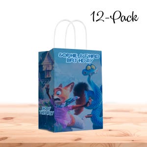 以下が含まれることがあります： 白い持ち手が付いたギフトバッグ12個パック。バッグには、漫画のキツネと青いヘビが描かれており、青い背景に「SOPHIE'S THIRD BIRTHDAY」と「ENJOY THE PARTY」の文字が書かれています。バッグは木製の表面にあります。