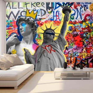 Può includere: Un murale vibrante con arte di graffiti e statue iconiche. L'opera d'arte include una raffigurazione di David con una corona e un occhio che piange, e la Statua della Libertà. Lo sfondo è pieno di graffiti e testo colorati.