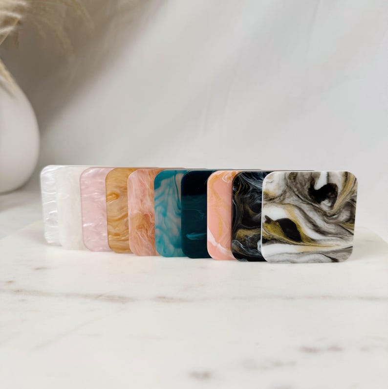 May include: A set of ten square-shaped hair clips in various colors and patterns, including white, pink, gold, teal, and black with gold swirls.