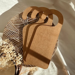 May include: Three brown cardboard door hangers with a rounded top and a cut-out handle. The hangers are stacked on top of each other.