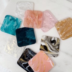 May include: Assortment of square coasters with marbled patterns in various colors, including white, pink, teal, gold, black, and gray.