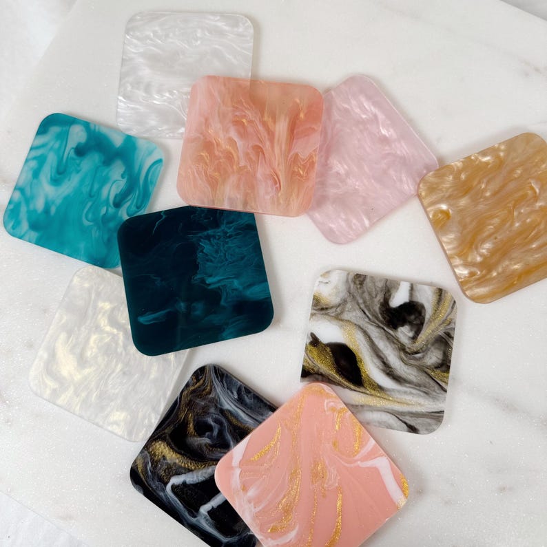 May include: Assortment of square coasters with marbled patterns in various colors, including white, pink, teal, gold, black, and gray.