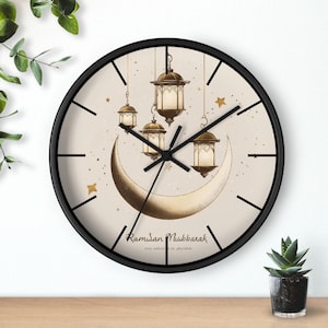 May include: A black round clock with a white face and gold accents. The clock features a crescent moon and hanging lanterns with the text "Ramadan Mubarak" and "May this month fill you with peace."