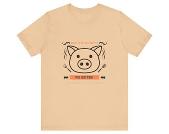 May include: A beige t-shirt with a black and white illustration of a pig's head with the text "Ready to get spit roasted" and "Pig Bottom" on the front.