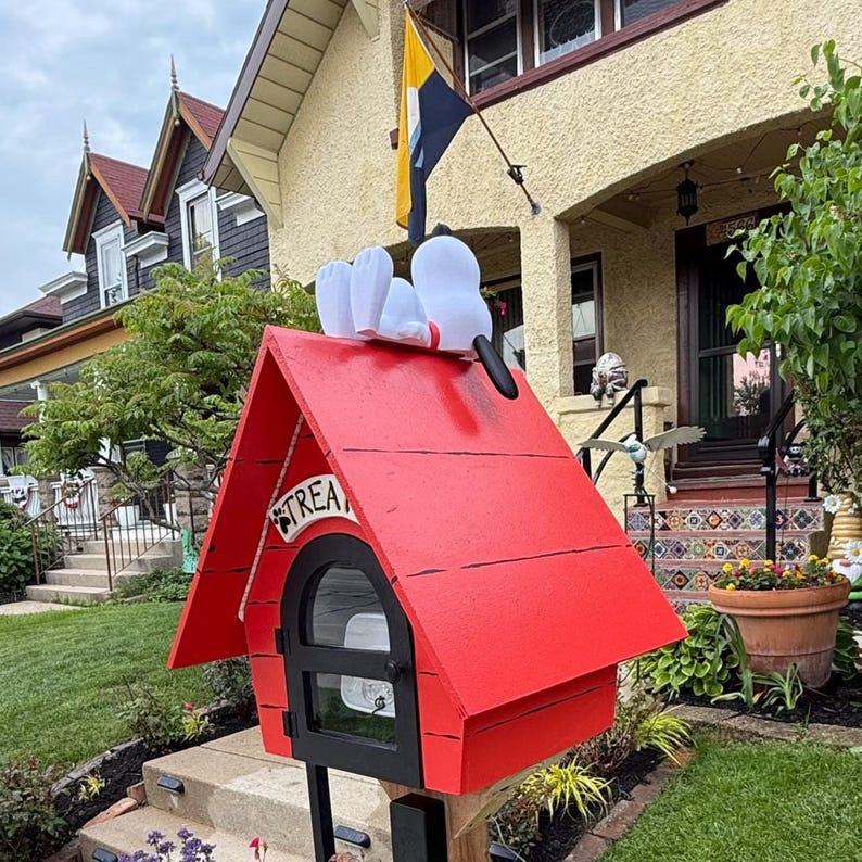 May include: A bright red wooden doghouse with a black arched door and a white sign reading TREATS. A white cartoon dog figure with black ears lies on the peaked roof. The structure is mounted on a post and features a small window in the door.